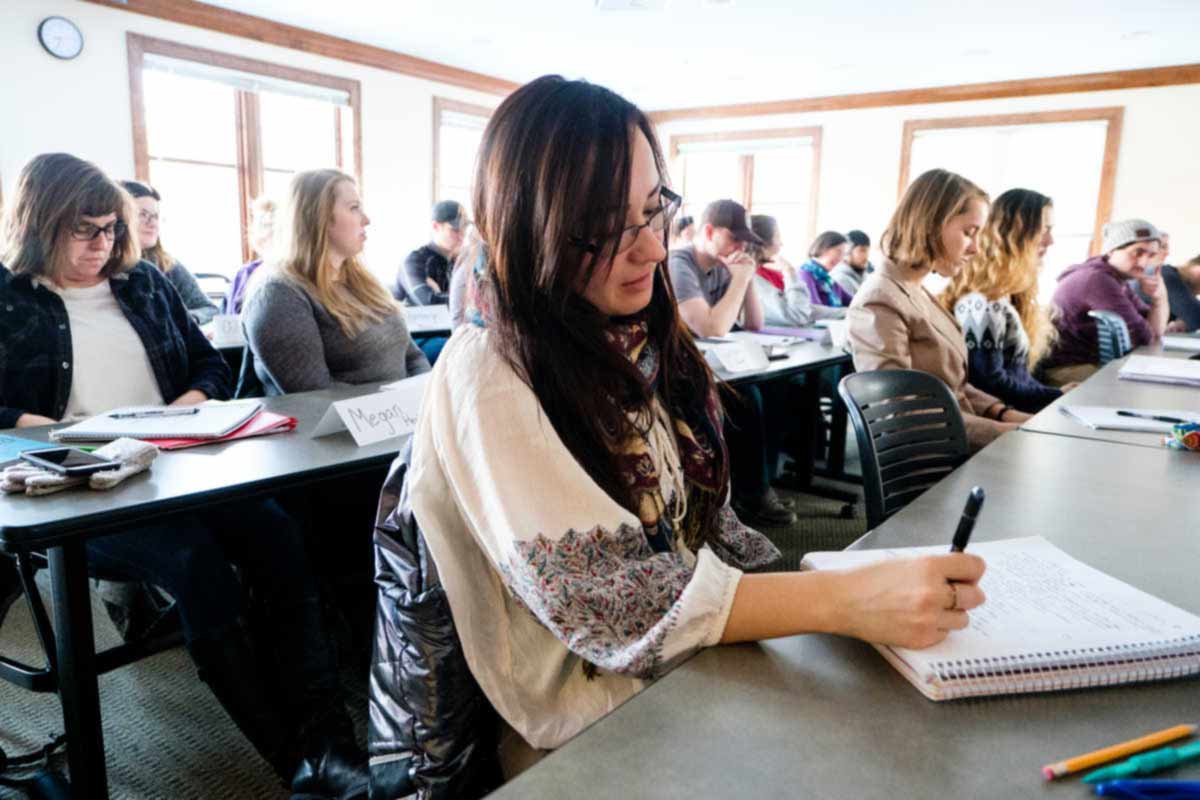 Photo of a female student taking notes during a lecture in a classroom. 